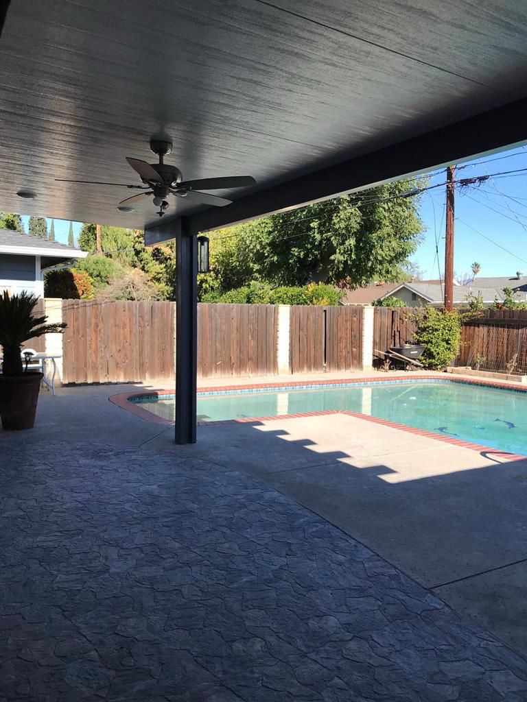 View of pool area from covered patio with ceiling fan.